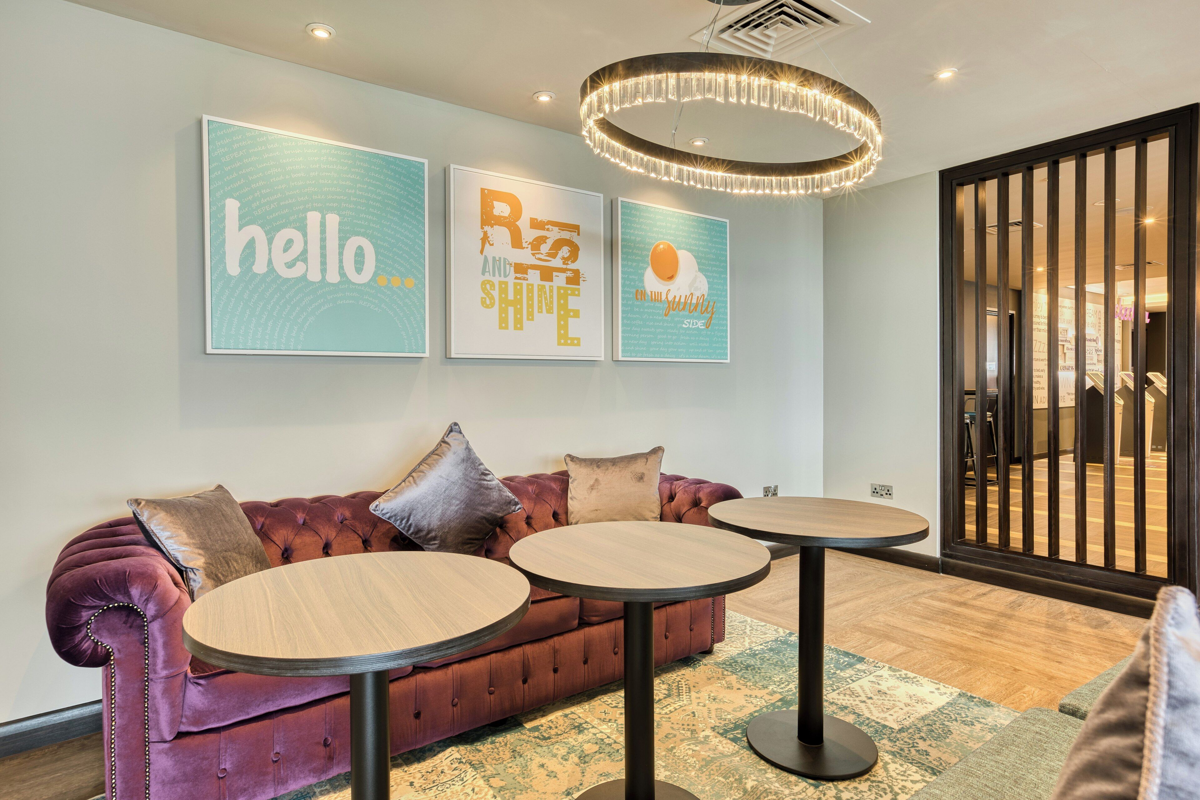 Ein stilvoller Lounge-Bereich mit einem üppigen roten Sofa, zwei runden Tischen und drei gerahmten Motivationspostern an der Wand.