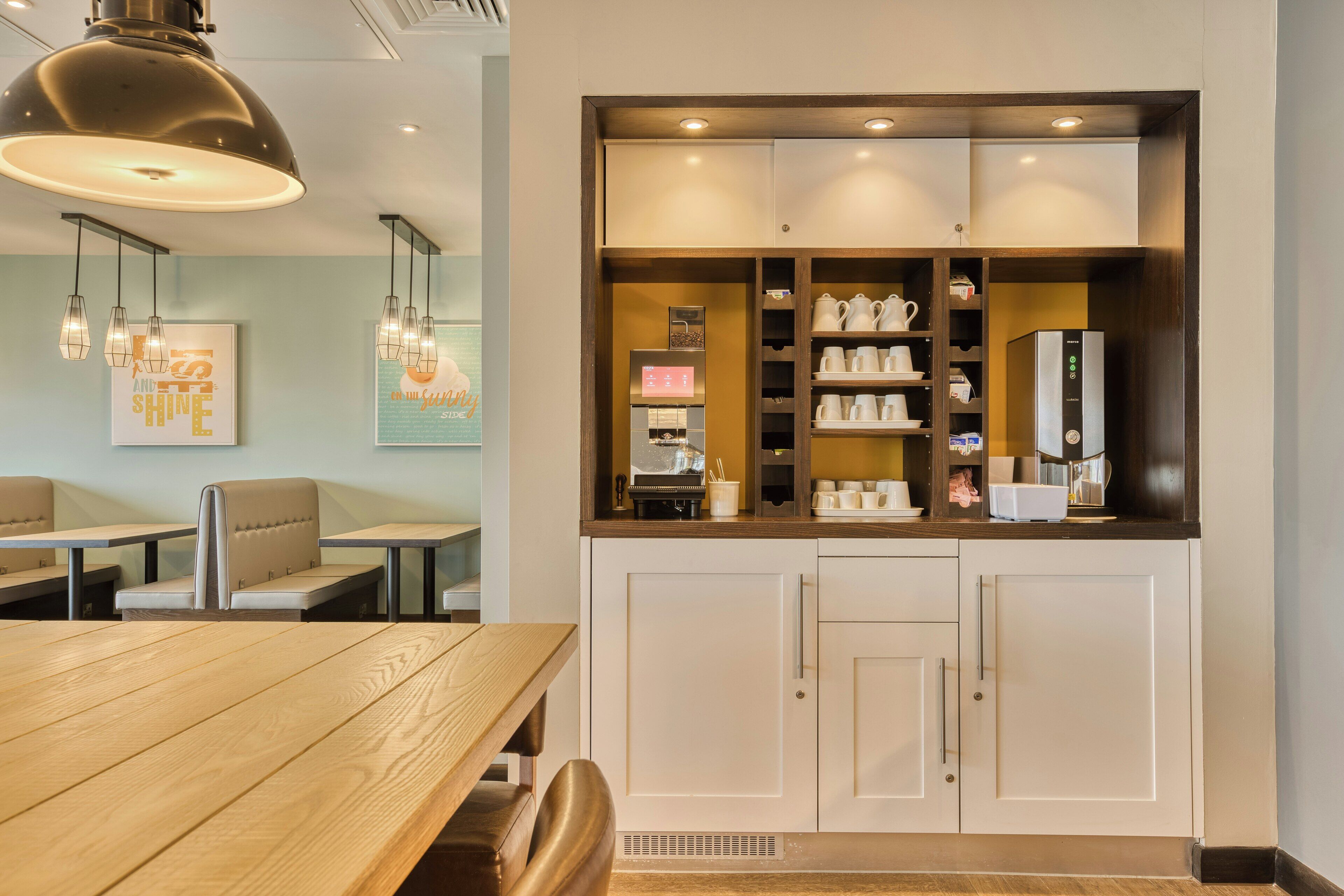 A restaurant with a wooden table and chairs, a coffee machine, and a wall with framed artwork.