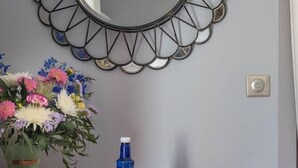 A mirror with a geometric frame, a vase of flowers, and a blue bottle on a wooden dresser. - Hôtel Palacito (Biarritz)