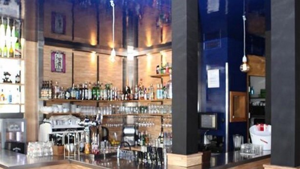 A bar area with a checkered floor, wooden bar counter, and white bar stools. - Hôtel Palacito (Biarritz)