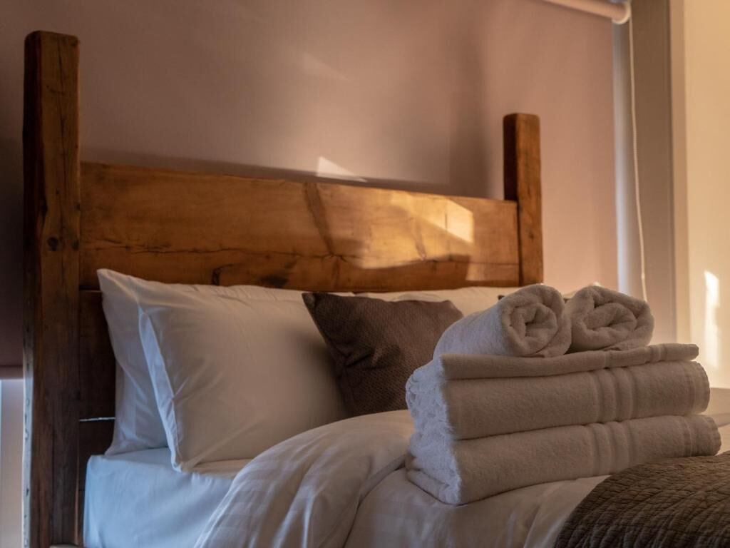 A bed with white linens, a wooden headboard, and a stack of folded towels.