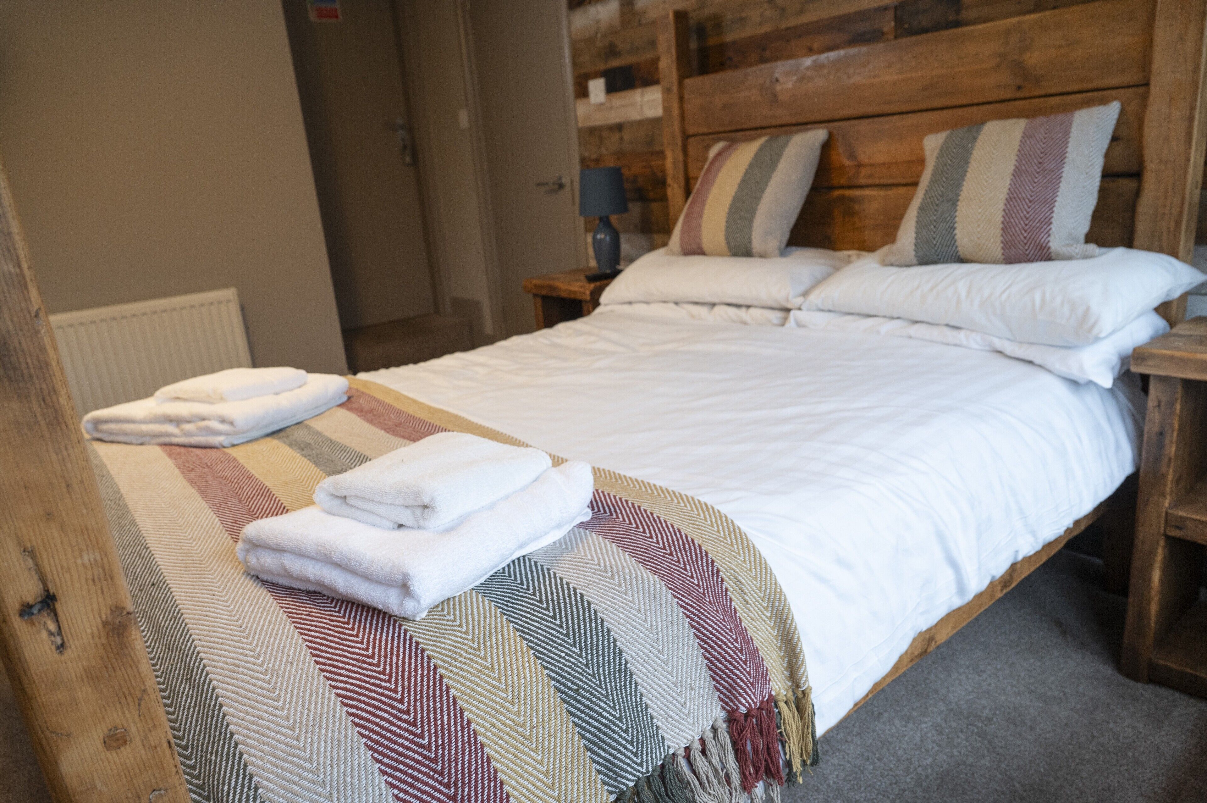 A neatly made bed with a striped blanket and pillows, a wooden headboard, and a small bedside table with a lamp.