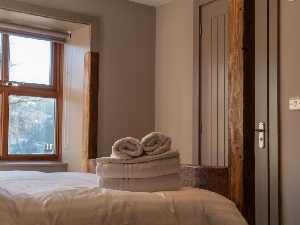 Una habitación de hotel con una cama, un ventanal, un pilar de madera y una puerta.