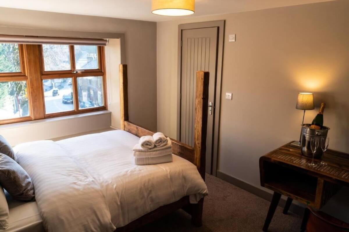 Un dormitorio con cama, mesita de noche con lámpara, puerta de madera y ventana con vista a la calle.