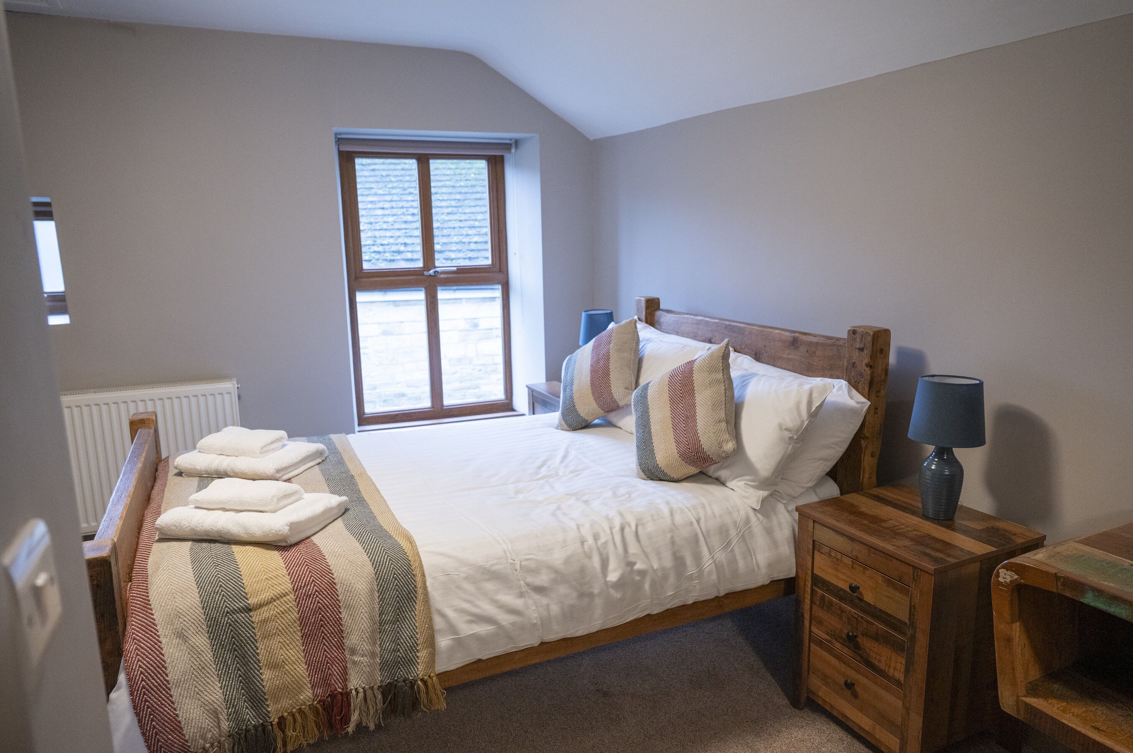 Une chambre avec un grand lit, une table de chevet en bois, une fenêtre et un radiateur.