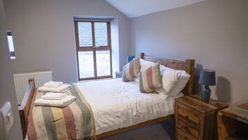 Une chambre avec un grand lit, une table de chevet en bois, une fenêtre et un radiateur.
