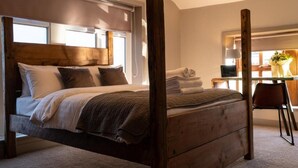 Un dormitorio con una cama con dosel de madera, un escritorio pequeño con una silla y una ventana con persianas.