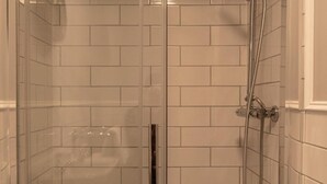 Ducha a pie con paredes de azulejos blancos y puerta de cristal.