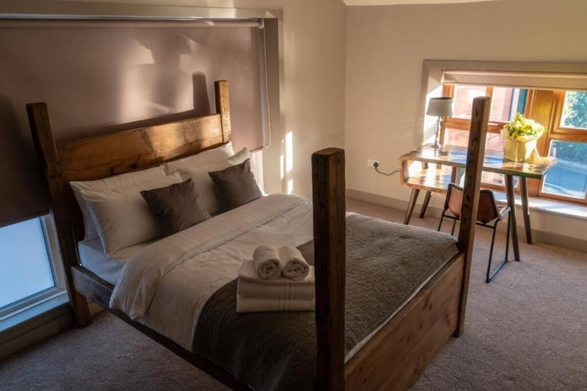 Un dormitorio con una cama con dosel de madera, una mesita con lámpara y una ventana con vistas.