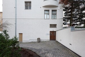 A building with a white exterior, a paved courtyard, and a door with a sign. - Forenom Premium Apartments Turku City (Turku)
