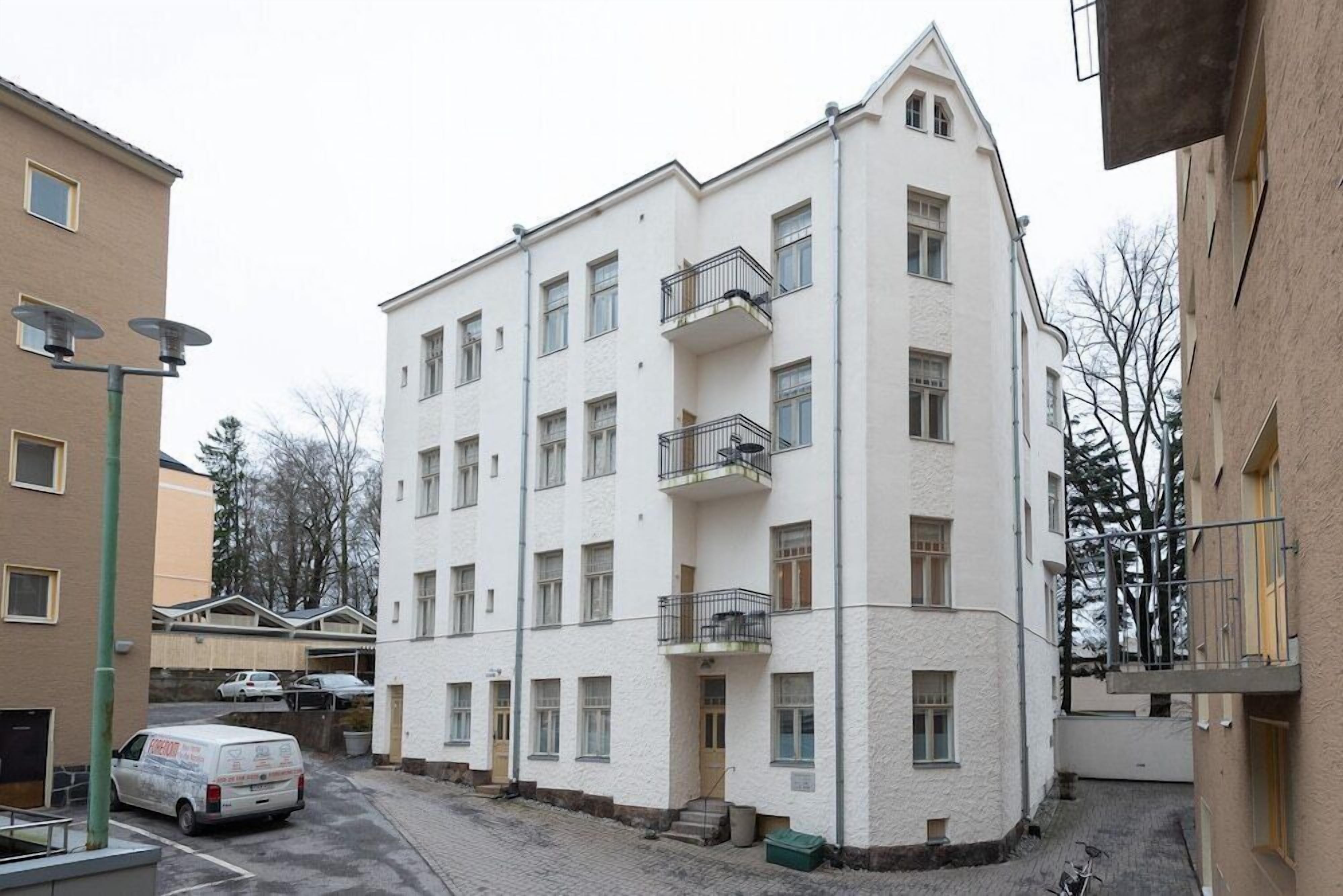 Ein mehrgeschossiges Wohngebäude mit Balkonen, einem Parkplatz und einem davor stehenden Lieferwagen.