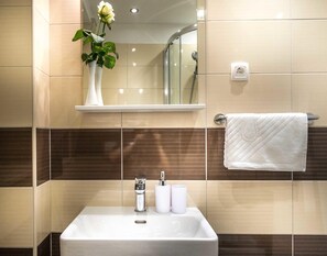 A bathroom with a white sink, a mirror above it, a towel rack, and a vase with a flower on a shelf. - Split Oasis Apartments (Split)