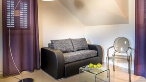 A modern living room with a black sofa, a glass coffee table with apples, a clear chair, and purple curtains. - Split Oasis Apartments (Split)