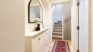 A hallway with a white vanity, a mirror, and a staircase leading to another room. - Elegant Pimlico Townhouse (London)