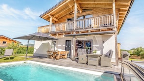 Een chalet met twee verdiepingen, een balkon, een zwembad en buitentafels.