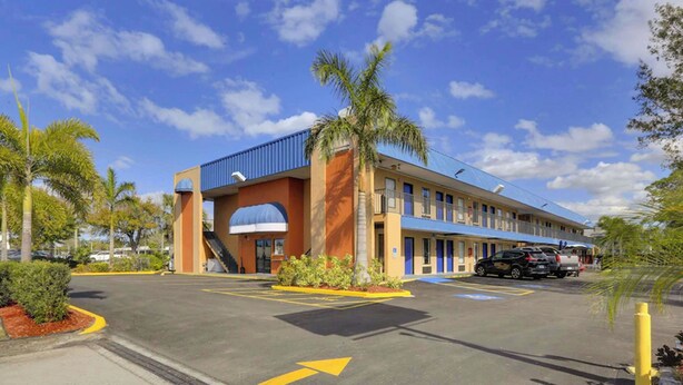 A motel with a blue and orange facade, a central archway, and a parking lot with directional arrows. - M-star Bradenton (Bradenton)