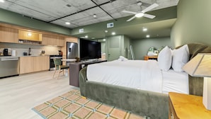 Une chambre d’hôtel moderne équipée d’une kitchenette, d’un lit, d’un bureau et d’un ventilateur de plafond.