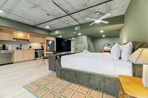 Une chambre d’hôtel moderne équipée d’une kitchenette, d’un lit, d’un bureau et d’un ventilateur de plafond.