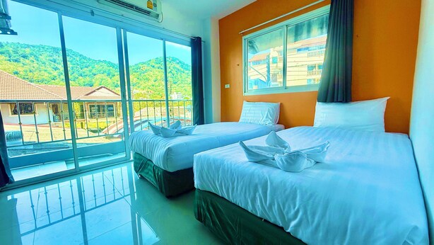 A hotel room with two beds, large windows, and a view of a hillside. - Silver Oaks Guest House (Patong)