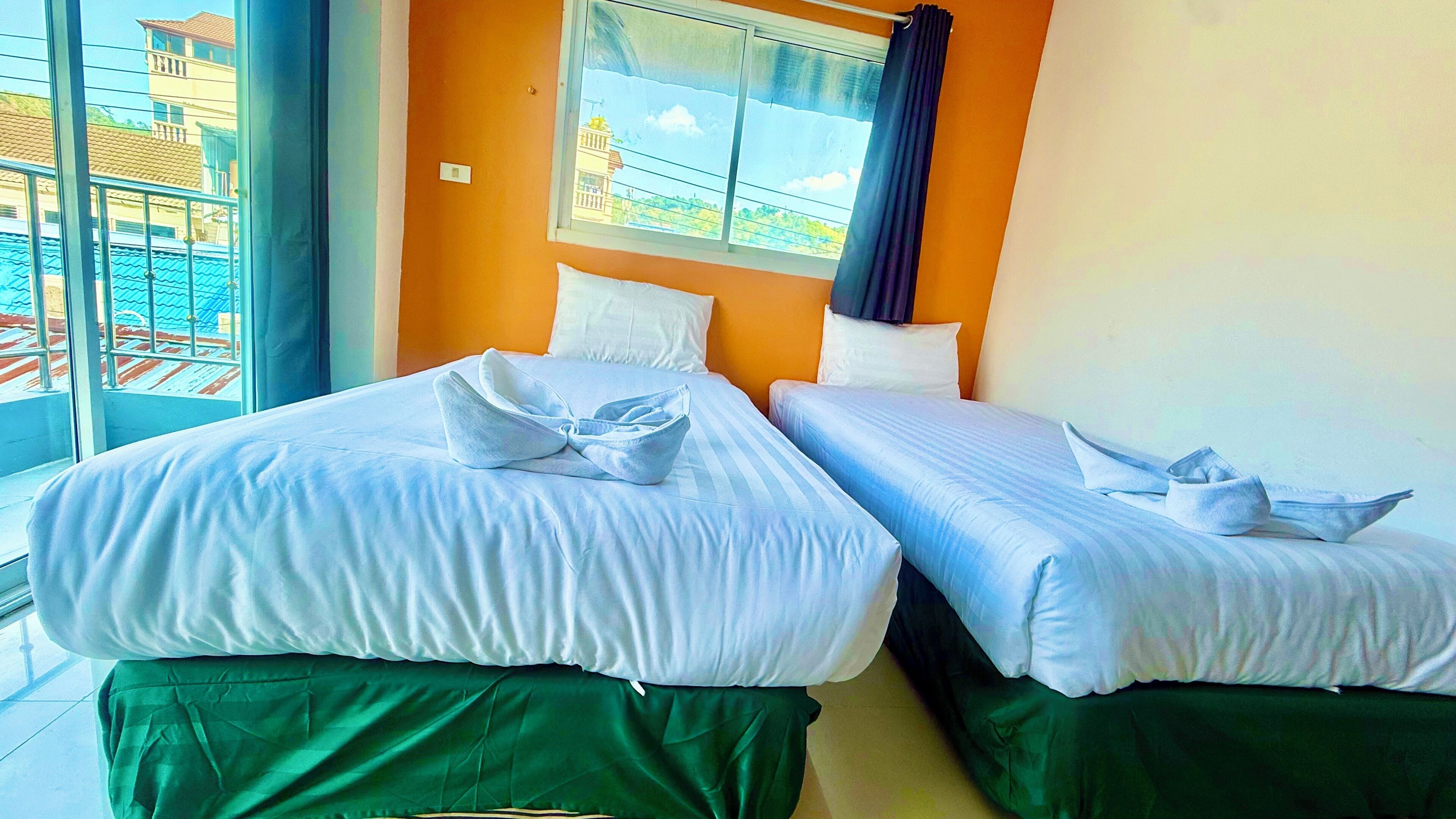 Een hotelkamer met twee bedden, een groot raam met uitzicht op gebouwen en een balkon met een hekwerk.