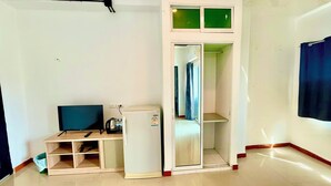 A compact room with a wooden desk, a small refrigerator, a television, and a sliding glass door closet. - Silver Oaks Guest House (Patong)