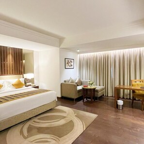A hotel room with a bed, a sofa, a dining table, and a large window with curtains. - Aditya Park A Sarovar Portico Hotel (Hyderabad)