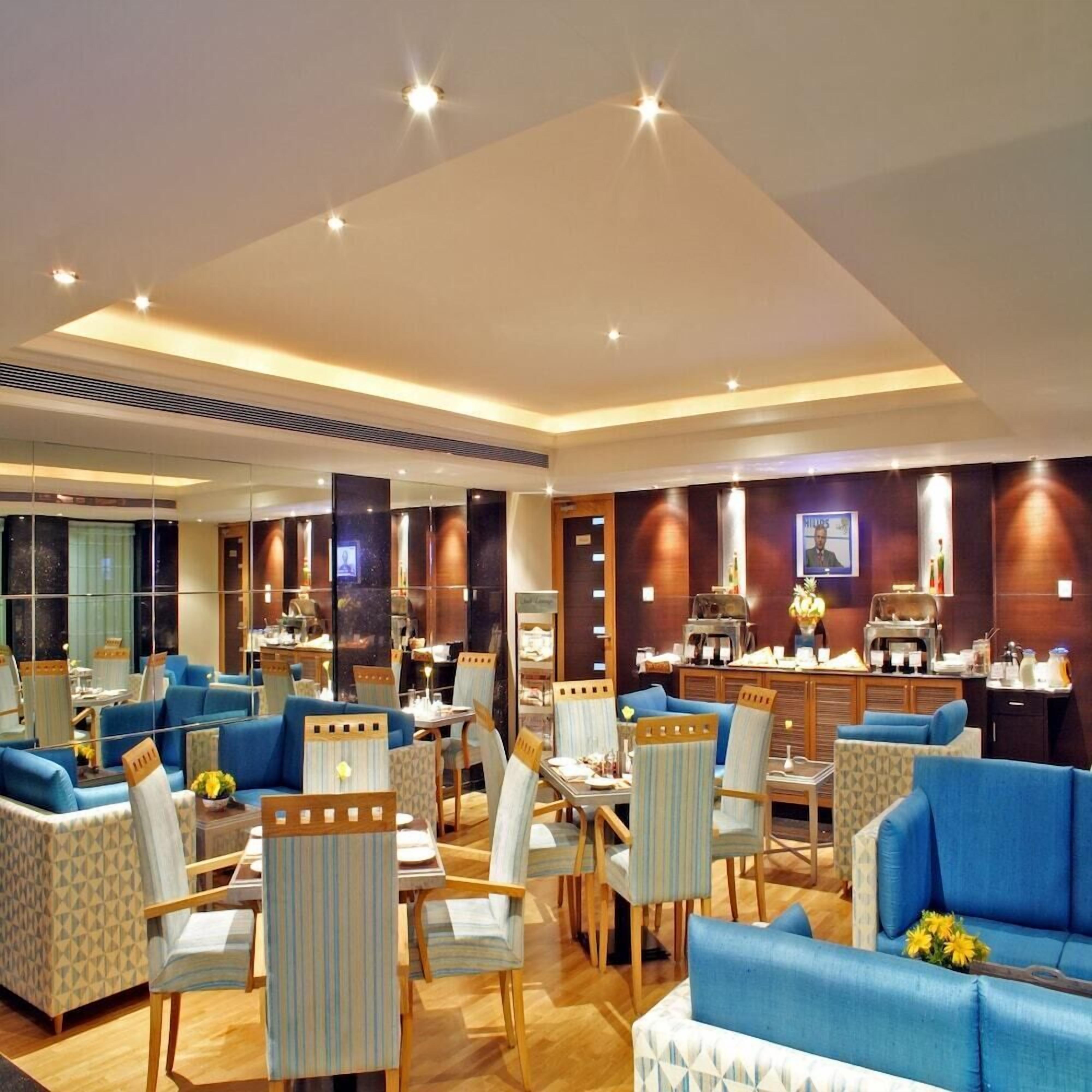 A modern hotel lobby with blue sofas, striped chairs, and a coffee station.