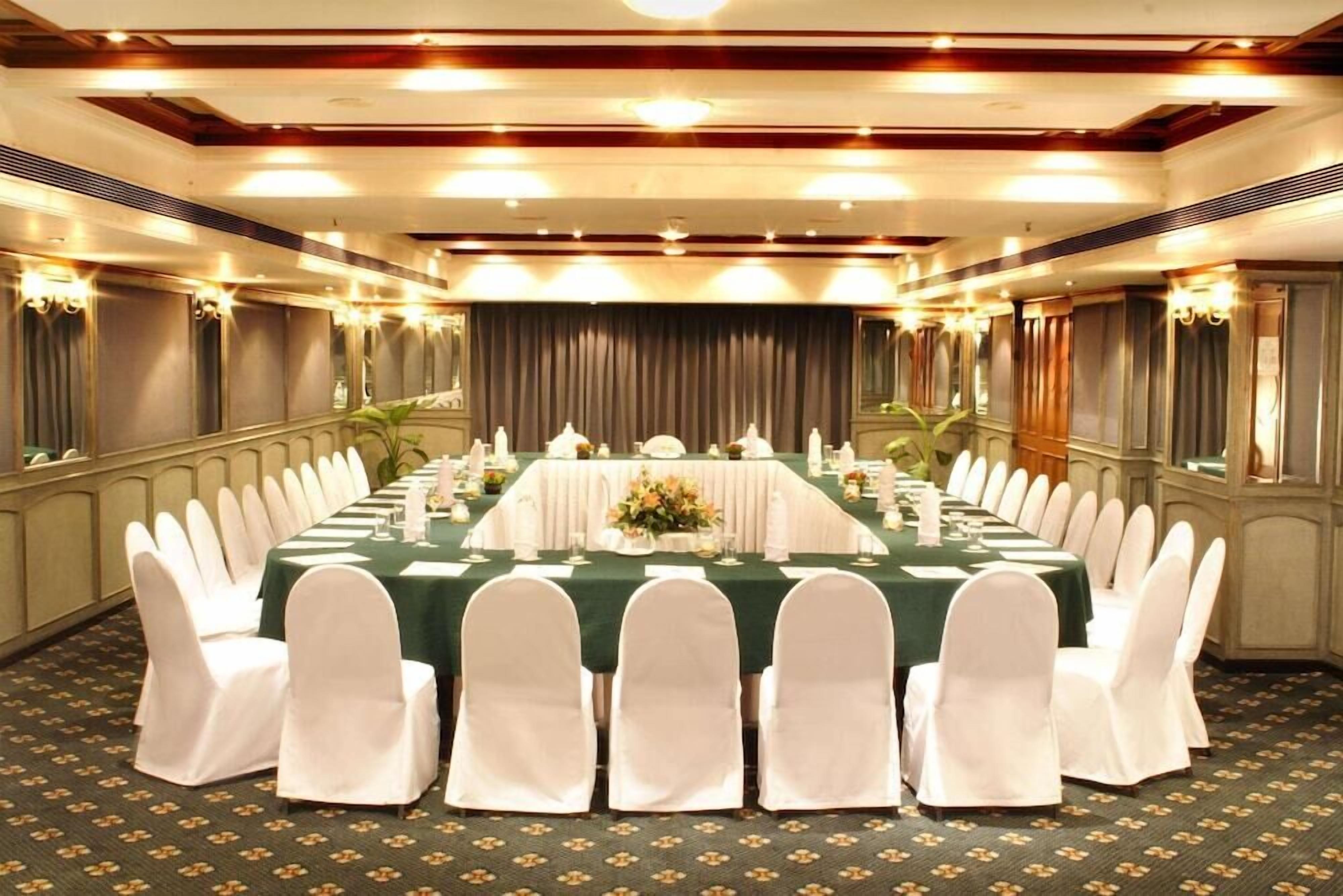 A banquet hall with a long table set for a formal event, surrounded by white chairs.