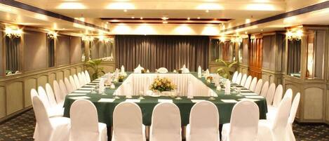 A banquet hall with a long table set for a formal event, surrounded by white chairs.