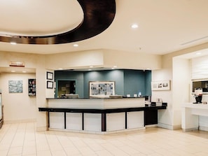 Un moderno vestíbulo de hotel con una recepción central, obras de arte enmarcadas en las paredes y un piso de baldosas impecable.
