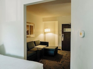 Habitación de hotel con cama, sofá, una mesita, lámpara y una puerta con cerradura.