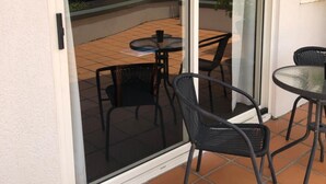 Un espace patio doté d’une porte vitrée donnant sur un balcon, aménagé avec deux tables rondes et quatre chaises.
