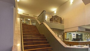 Eine Treppe mit Glasgeländer führt zu einer zweiten Etage, einem Empfangstresen und einer Wand mit gerahmten Zertifikaten.