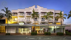 Ein mehrstöckiges Hotel mit Balkonen, einem zentralen Eingang und Palmen.