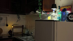 Una cocina con un refrigerador, un lavamanos y varios objetos sobre la encimera, incluyendo una botella de licor y un cartel.