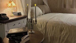 Un dormitorio con cama a dosel, una mesita de noche con lámpara y un tocador con libros y teléfono.