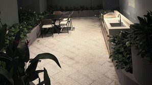 Un patio al aire libre con una mesa y sillas para comer, rodeado de plantas en macetas.