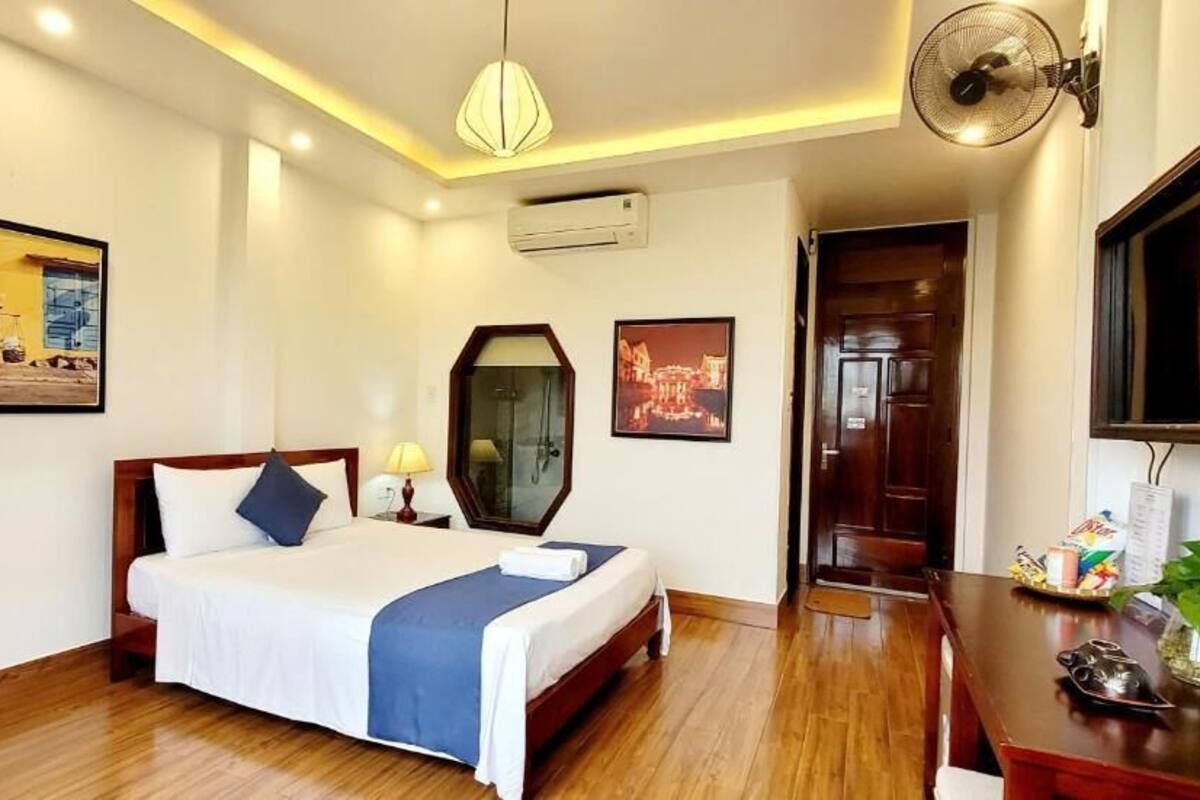 A hotel room with a bed, bedside table, lamp, air conditioning unit, and a wall-mounted TV.