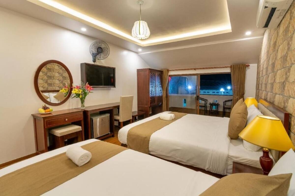 A hotel room with two beds, a desk, a chair, a TV, and a window with a night view.