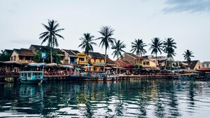 A waterfront area with traditional buildings, palm trees, and a dock with boats. - The Linh Hoi An (Hoi An)