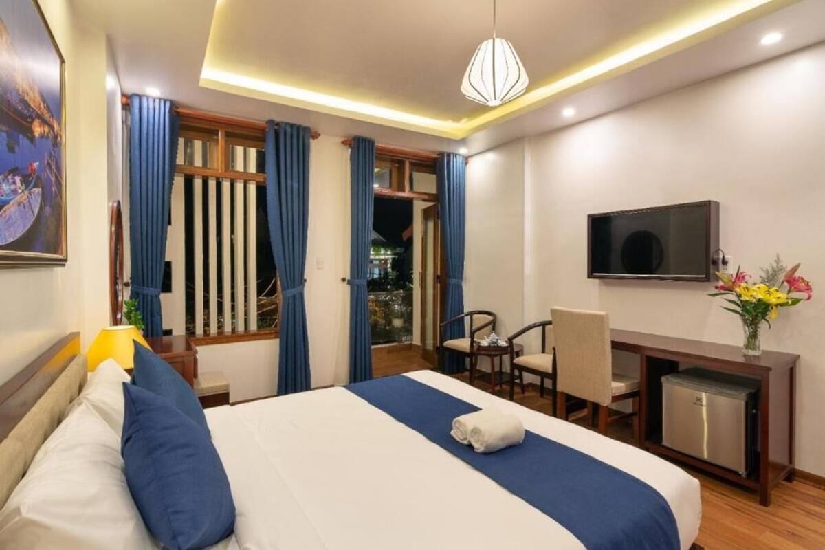 A hotel room with a bed, a desk with a TV, a chair, and a small fridge.