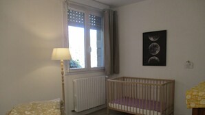 Quarto com berço, janela com persianas, radiador e quadro fixado na parede.