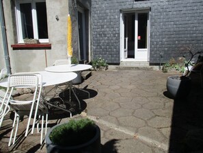 A patio with outdoor furniture, a potted plant, and a building entrance. - La Source - Appartment & terrace - 90m2 - France, Auvergne Volcanoes Park (Orcival)