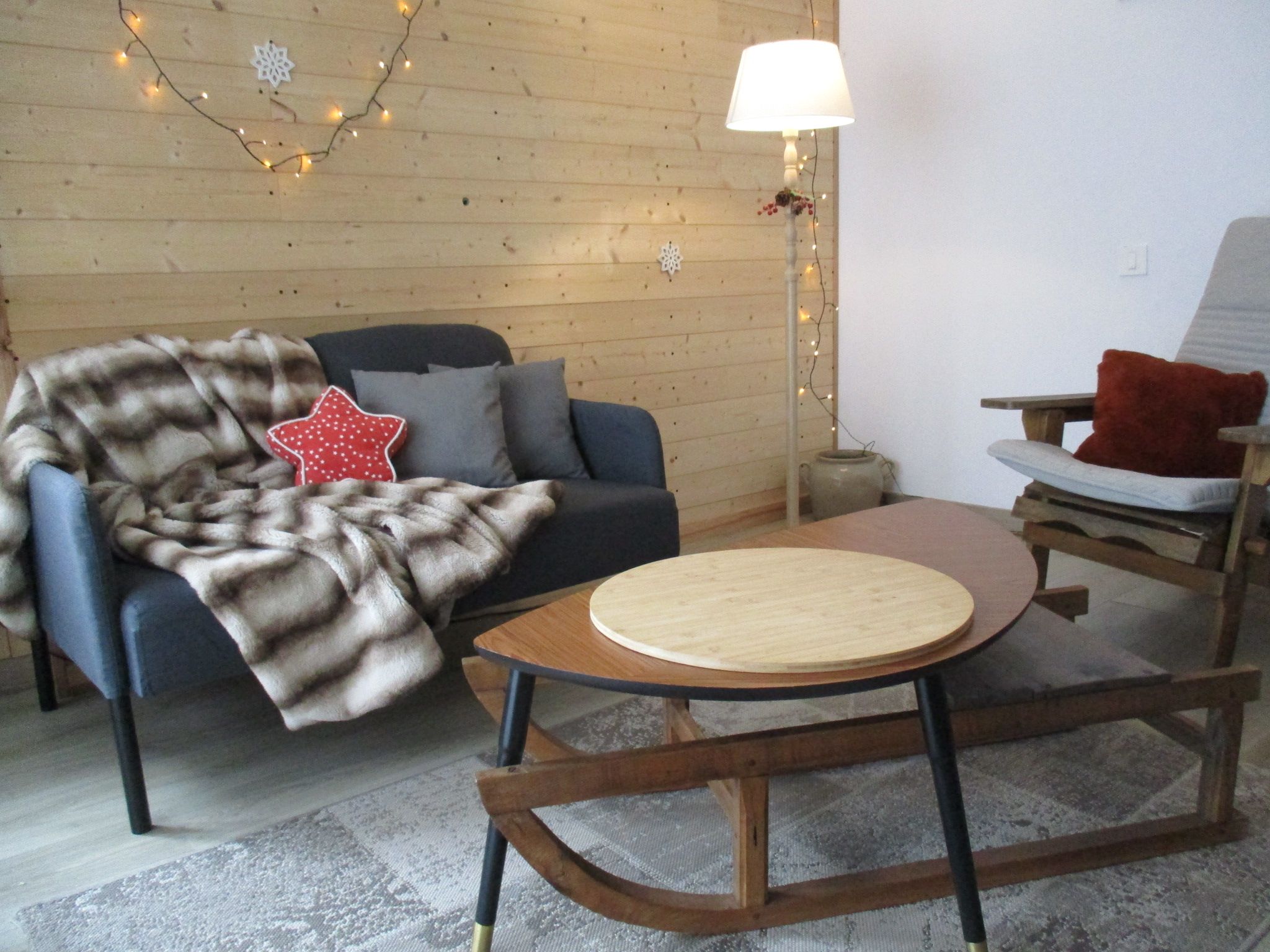 Een gezellige kamer met een houten vloer, een ronde houten tafel, een blauwe bank en een stoel met een rood kussen.