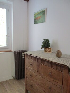 Ein Zimmer mit einem Holzkoffer, einem Heizkörper, einem Fenster und einem Wandbild.