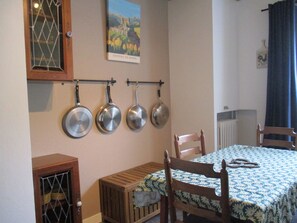 A dining area with a table covered in a floral tablecloth, wooden chairs, and a wall-mounted pan rack. - La Source - Appartment & terrace - 90m2 - France, Auvergne Volcanoes Park (Orcival)