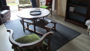 Um quarto com uma mesa de madeira redonda, duas cadeiras, um sofá, uma estante de livros e uma janela com cortinas.