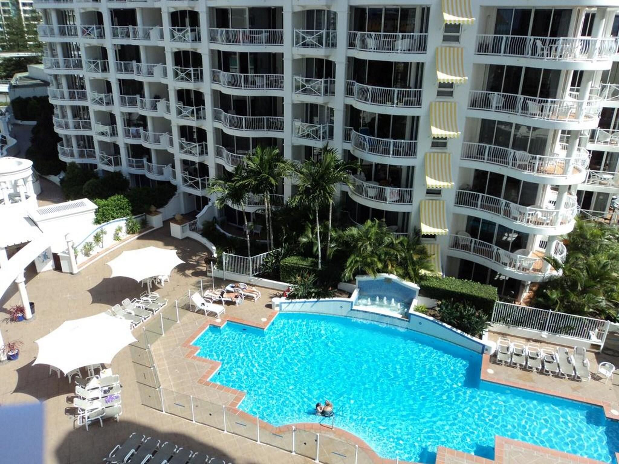 A multi-story hotel with a swimming pool surrounded by sun loungers and umbrellas.