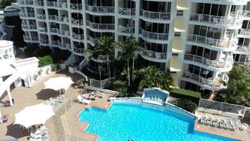 A multi-story hotel with a swimming pool surrounded by sun loungers and umbrellas.