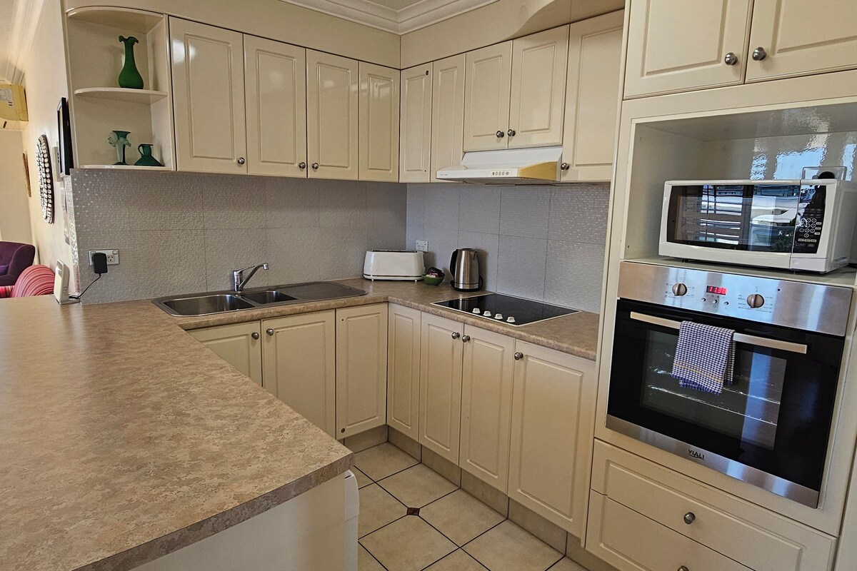 Una cocina con armarios color beige, un fregadero de acero inoxidable, un tostador y un microondas.